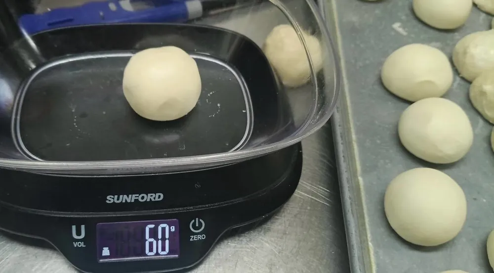 A flour dough ball on a kitchen scale reading 60 grams