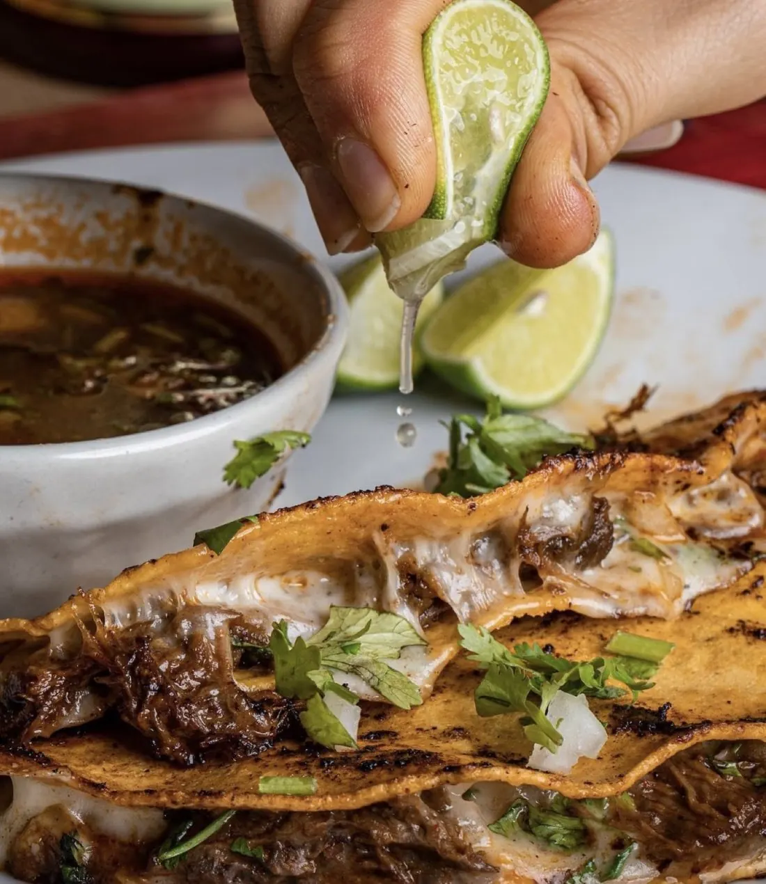 Quesabirria tacos with melted cheese, lime and consomé